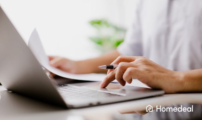 Man op laptop met pen in zijn hand en papieren ernaast