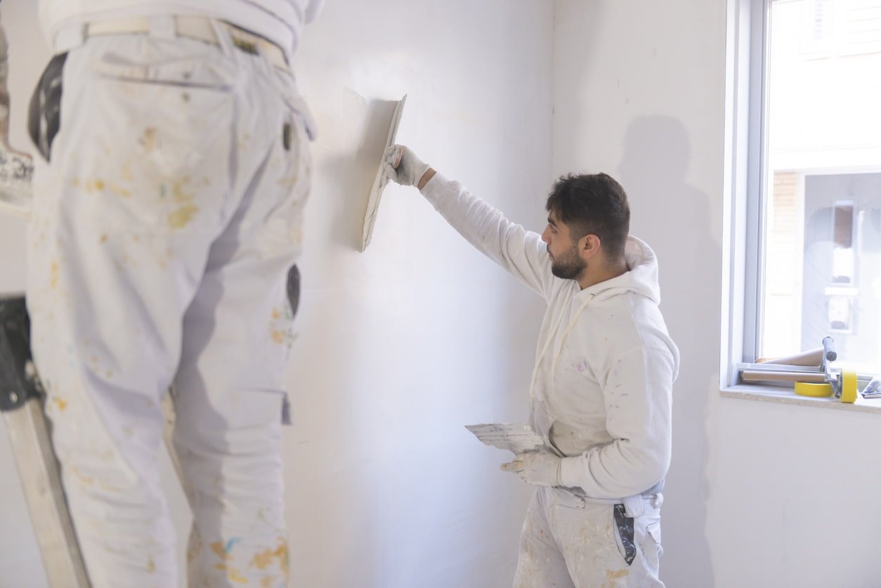 2 schilders die muur aan het stucen en schilderen zijn