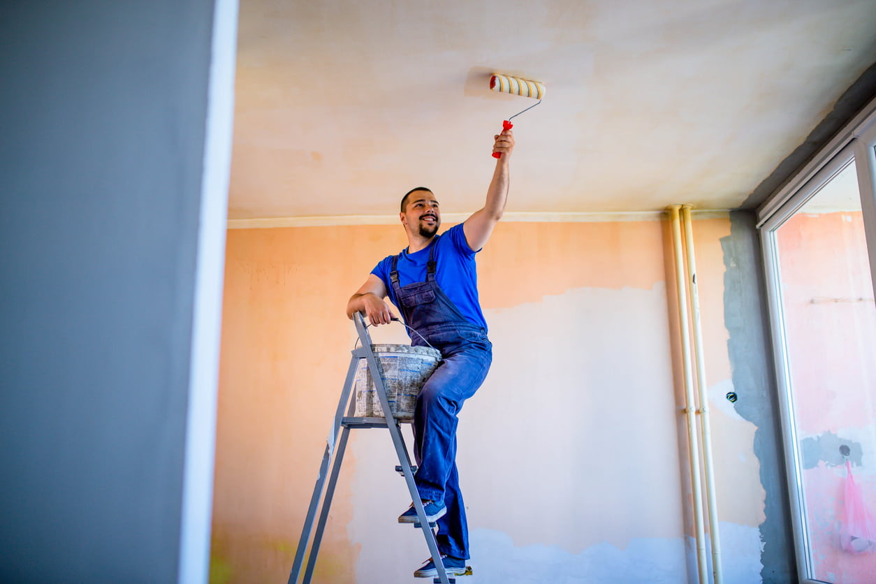 schilder met blauw shirt die plafond aan het schilderen is