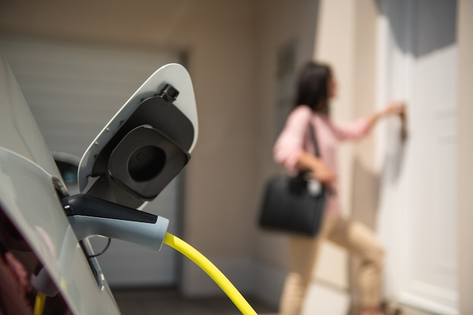 Een vrouw die ervoor heeft gekozen om een laadpaal te kopen voor thuis en haar auto nu thuis oplaadt.