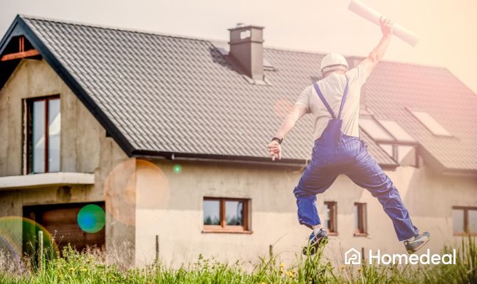 Springende aannemer met papieren in zijn hand voor een huis