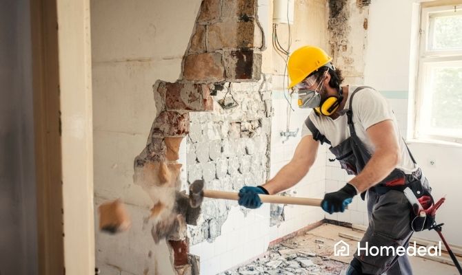 Een vakspecialist sloopt een muur tijdens de verbouwing van een huis.